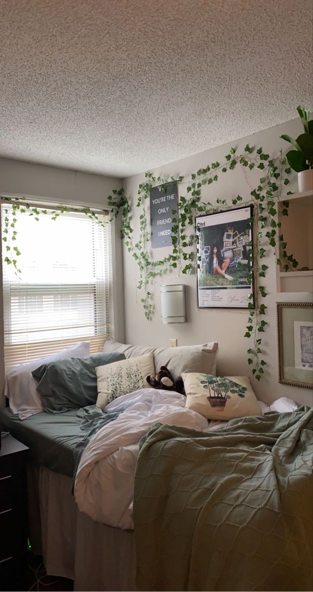 an unmade bed in a small room with plants on the wall and pictures above it