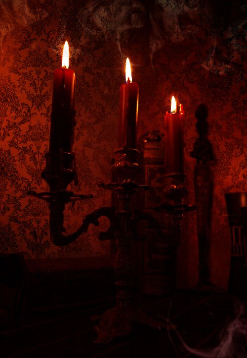 three candles are lit in the dark with red light coming from one candle and another on the wall