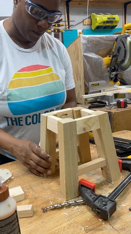 a woman working on a wooden stool in a shop with tools and woodworking equipment