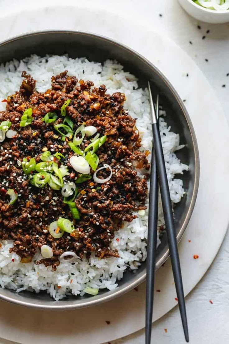 a bowl filled with rice and meat on top of a white plate next to chopsticks