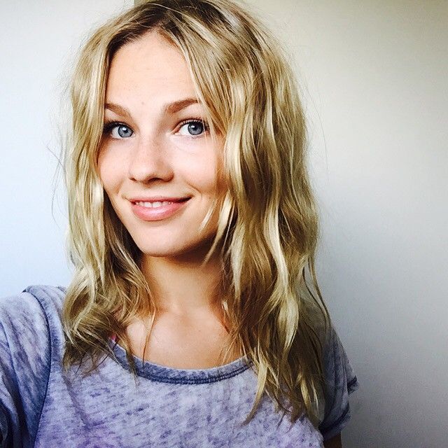 a woman with blonde hair and blue eyes smiles at the camera while standing in front of a white wall