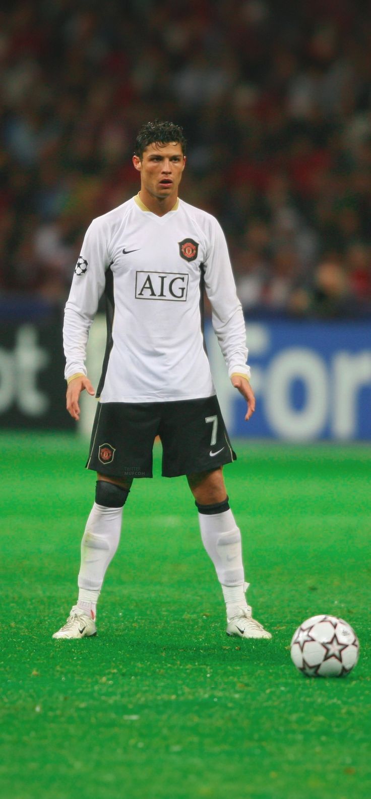 a soccer player standing next to a soccer ball on a field with spectators in the background