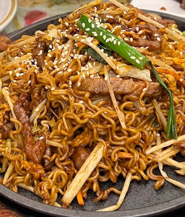 a plate full of noodles with meat, vegetables and sesame seeds on the side is sitting on a table