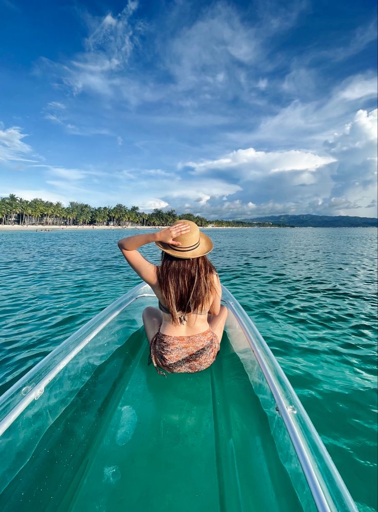 a woman sitting in the back of a boat looking out at the water and palm trees