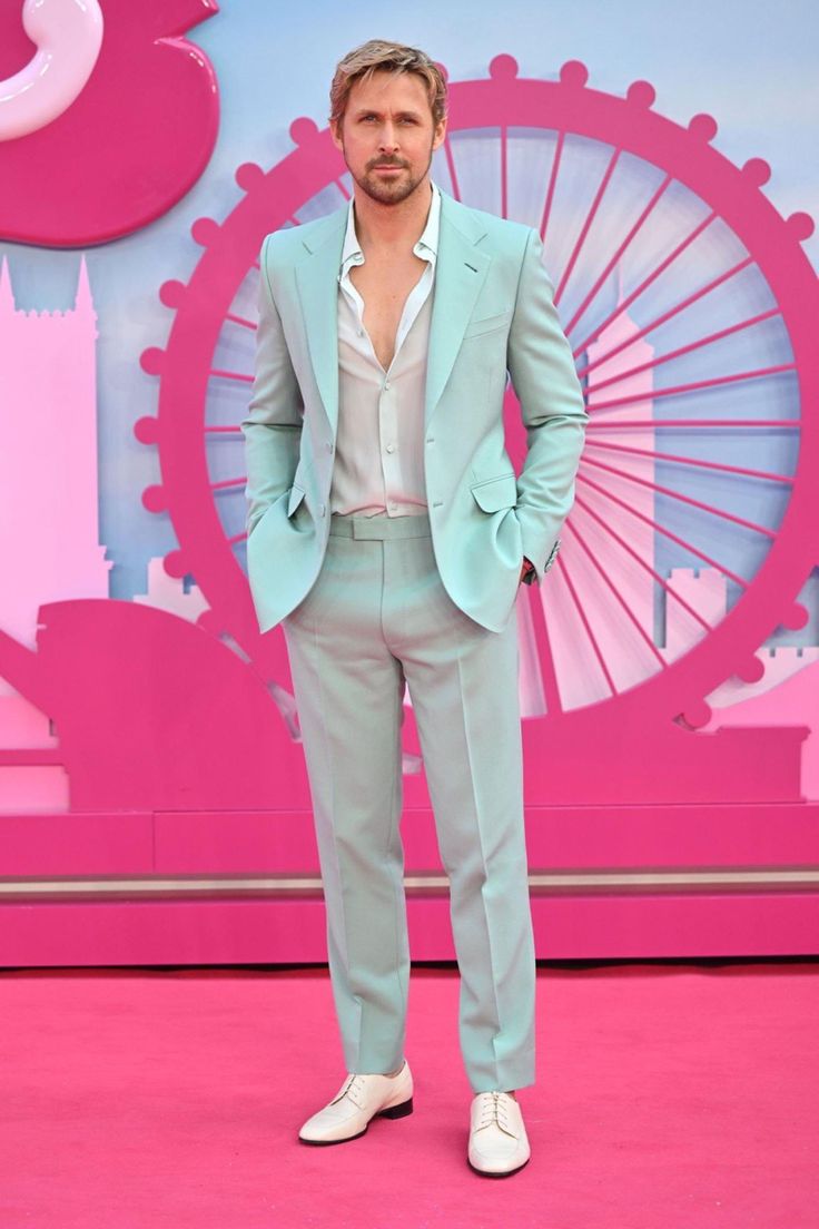 a man in a light blue suit and white shoes stands on a pink carpet with his hands in his pockets