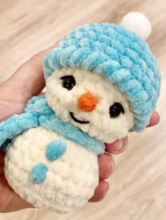 a hand holding a small stuffed snowman wearing a blue hat and scarf