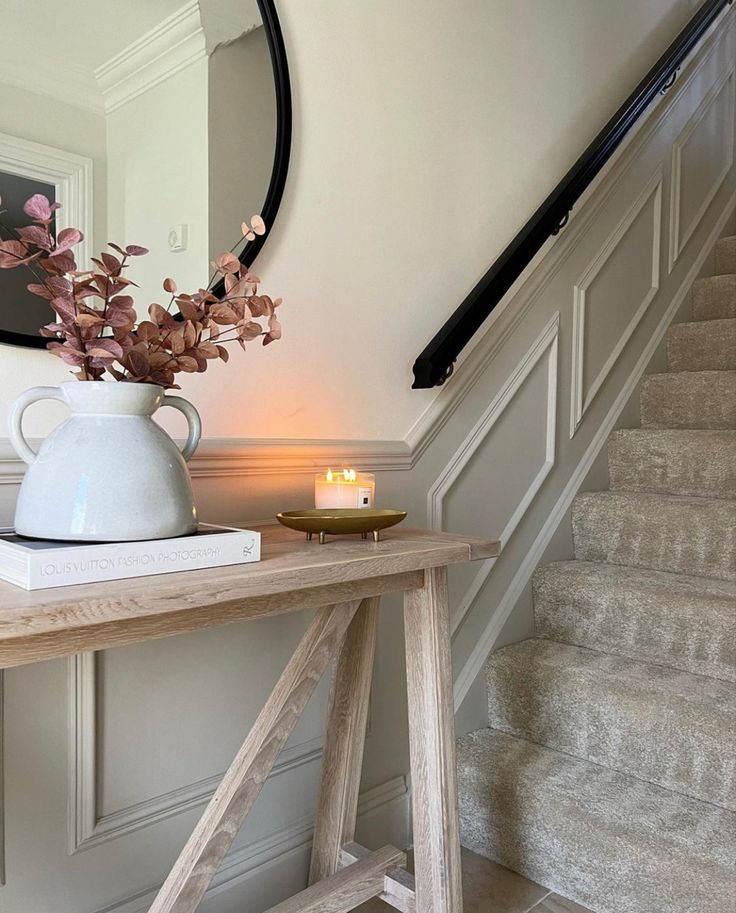 a table with a vase on top of it next to some stairs and a mirror