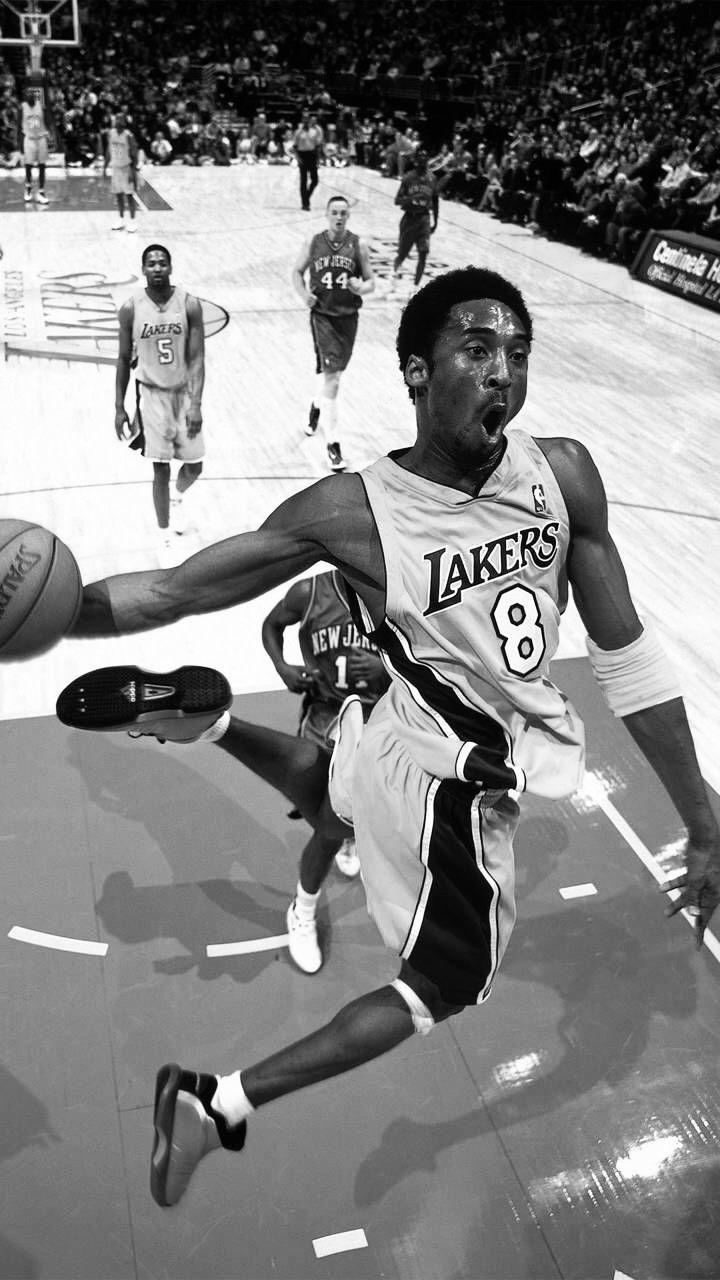 a basketball player is in mid air after going to the basket while other players are on the court behind him