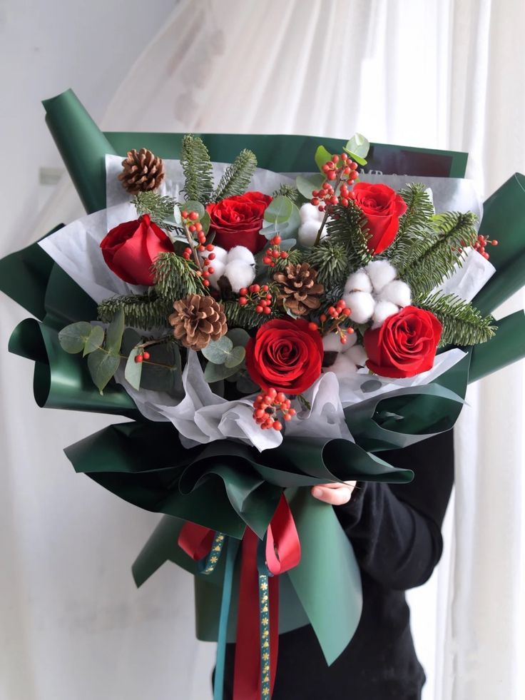 a woman holding a bouquet of red roses and greenery