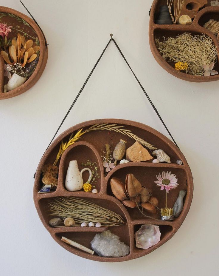 three clay pots are hanging on the wall with plants and rocks in them, along with other decorative items