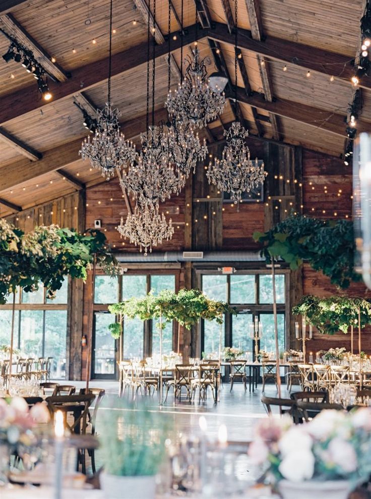 an indoor wedding venue with chandeliers hanging from the ceiling and greenery on the tables