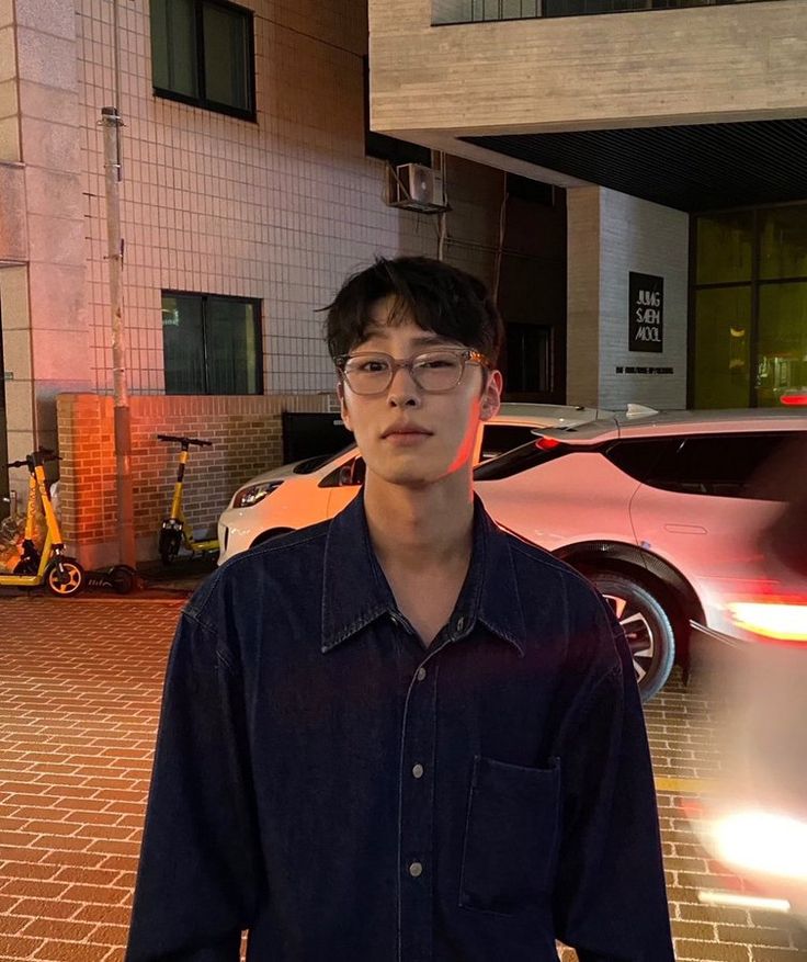 a young man standing in front of a car on a brick road next to a building