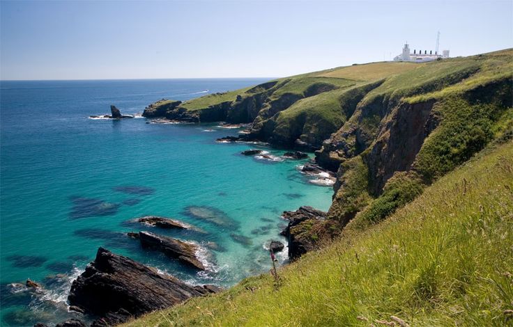 the ocean is blue and clear with green grass on the hill next to it's shore