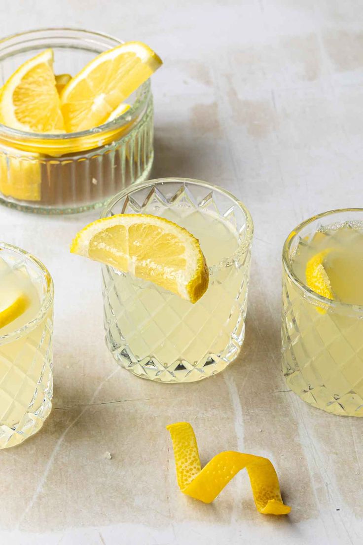 three glasses filled with lemonade sitting on top of a table next to sliced lemons