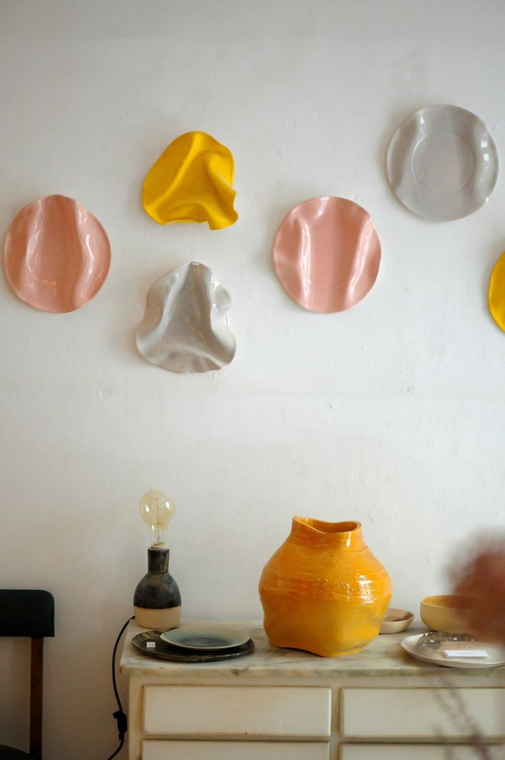 a white table topped with yellow and pink vases next to a wall mounted art piece