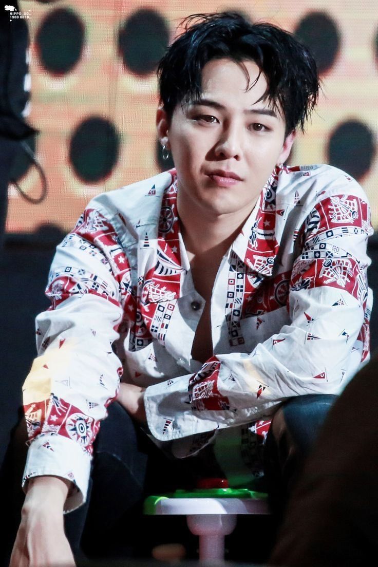 a man with black hair sitting down in front of a microphone and wearing a red and white shirt