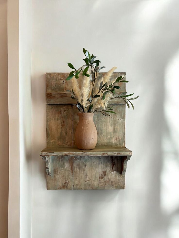 a wooden shelf with a vase on it and some plants in the bottom right corner