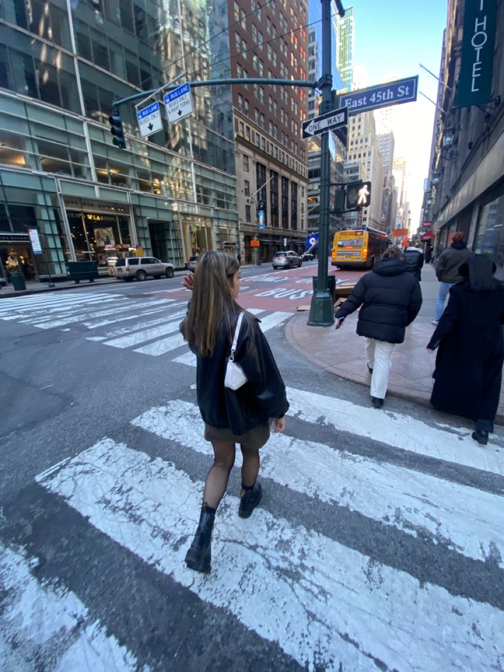 a woman walking across a crosswalk in the middle of a city with snow on the ground