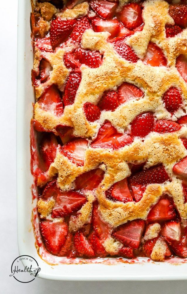 strawberry cobbler in a white baking dish topped with fresh strawberries