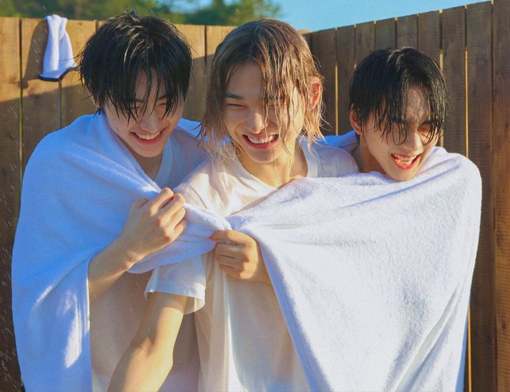 three young men wrapped in white towels standing next to each other on a wooden fence