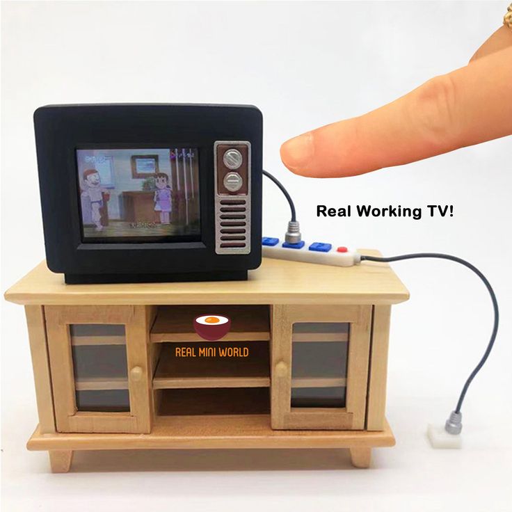 a hand is pointing at a toy tv set on top of a small table with a remote control