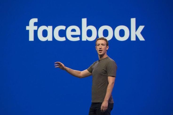 a man standing in front of a facebook sign with his hands out to the side