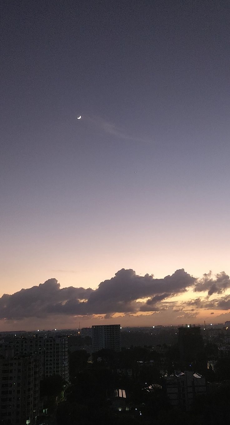 an airplane flying in the sky at night with clouds and city lights behind it as the sun is setting