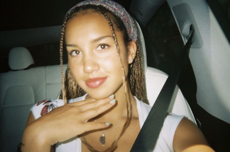 a woman sitting in the back seat of a car with braids on her hair