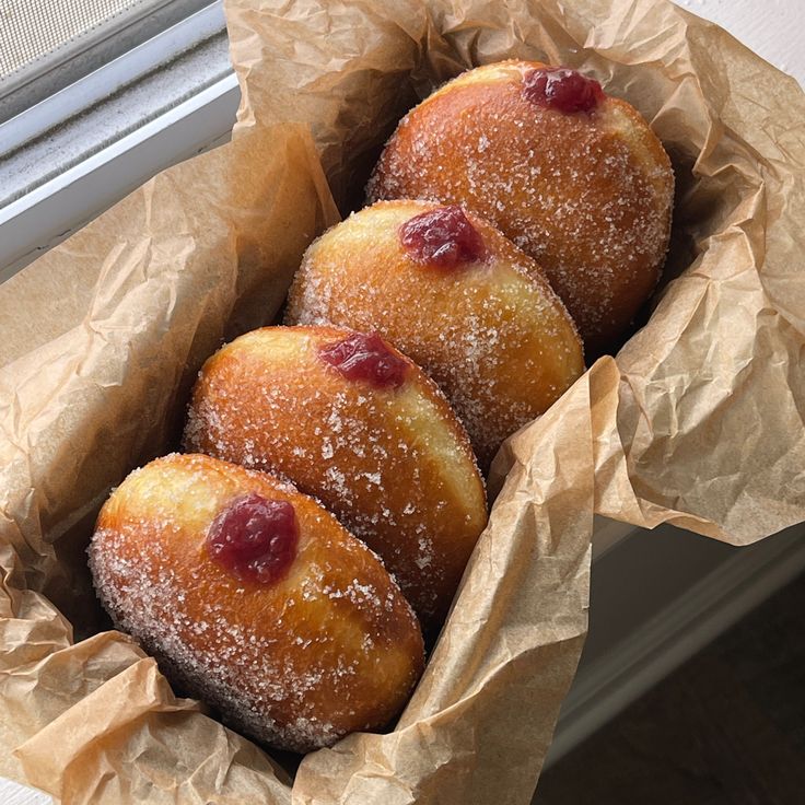 three doughnuts in a brown paper bag on a window sill next to a window