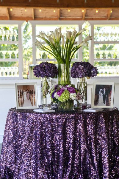 purple flowers in vases on a table with pictures and lights behind them at a wedding reception