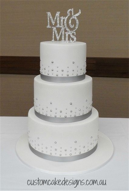 a three tiered white cake with silver decorations