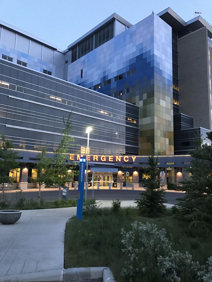 the entrance to an emergency department building lit up at night with trees and bushes in front