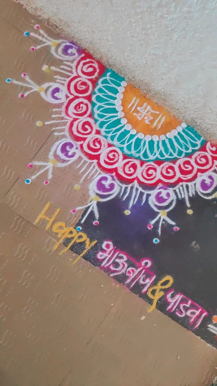 a colorful painting on the ground in front of a wall that says happy diwali