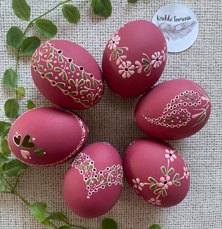 six pink painted eggs sitting on top of a table next to green leaves and a tag