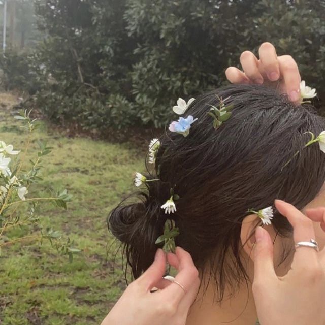 a woman with flowers in her hair is looking at the grass and bushes behind her