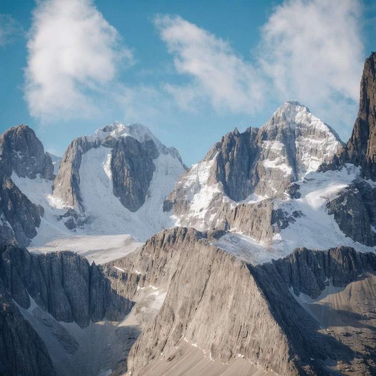 some very tall mountains with snow on them and clouds in the sky over them as seen from an airplane