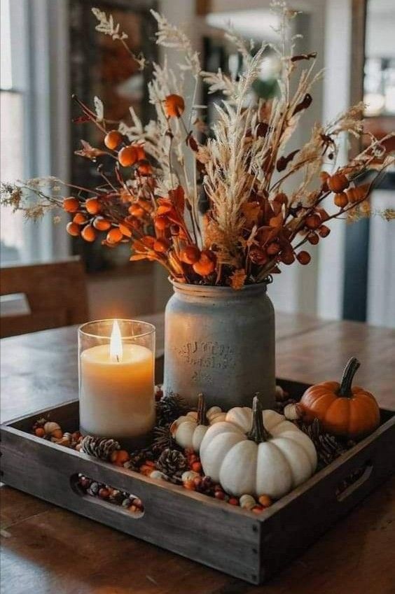 a candle is sitting on a tray with some flowers and pumpkins in the center