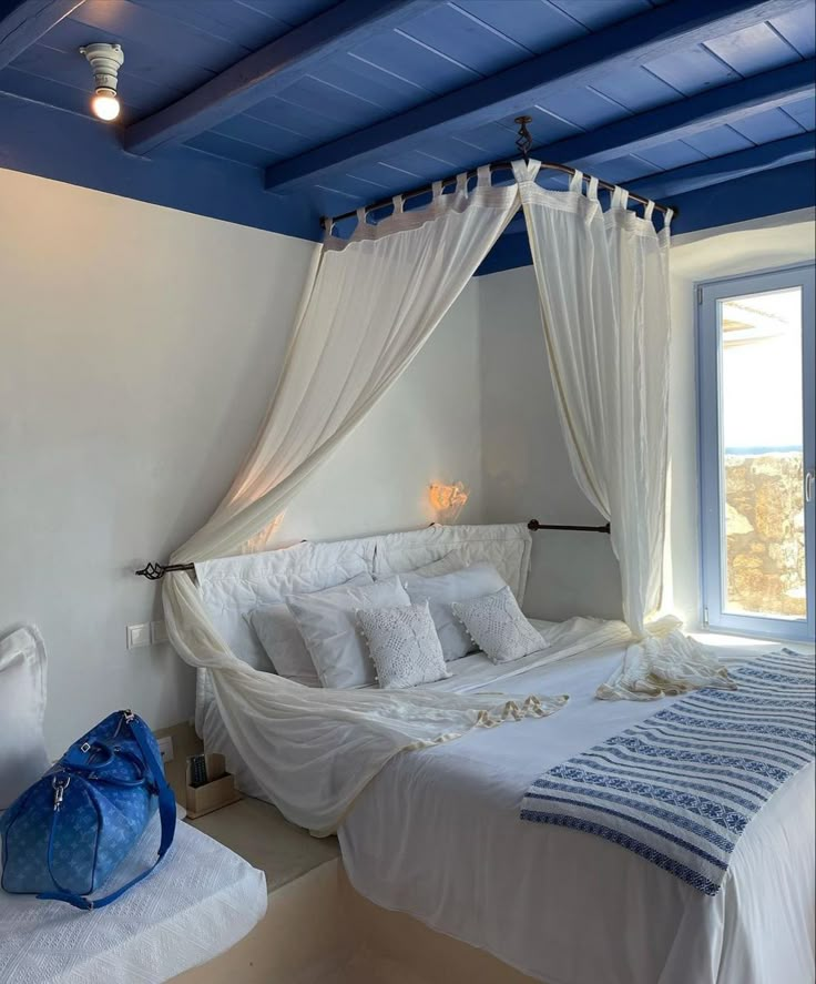 a white bed sitting under a window next to a blue painted ceiling in a bedroom