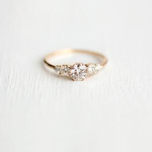 three stone diamond ring sitting on top of a white surface with light shining in the background