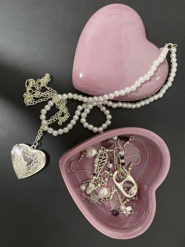 a pink heart shaped bowl with pearls and other jewelry items on it, next to a necklace holder