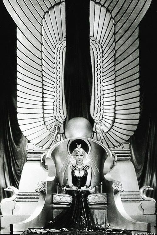 an old photo of a woman sitting on a chair in front of two large wings