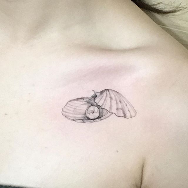 a woman's chest with a small tattoo of a shell and a seashell on it