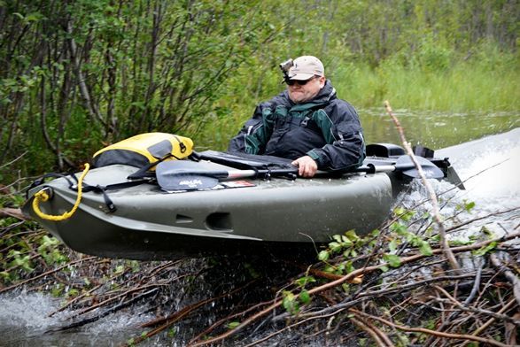 a man sitting on top of a kayak in the middle of a river next to trees