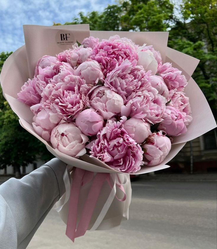 a bouquet of pink peonies is being held by a person's hand