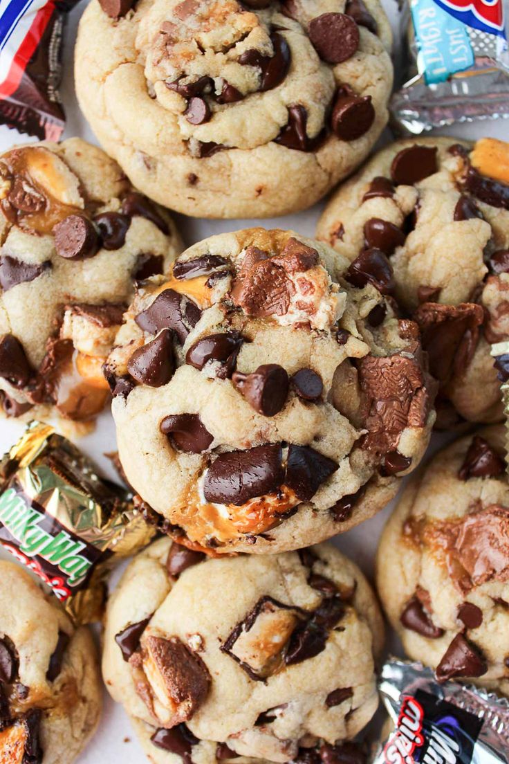 chocolate chip cookies are piled on top of each other with candy bars in the background