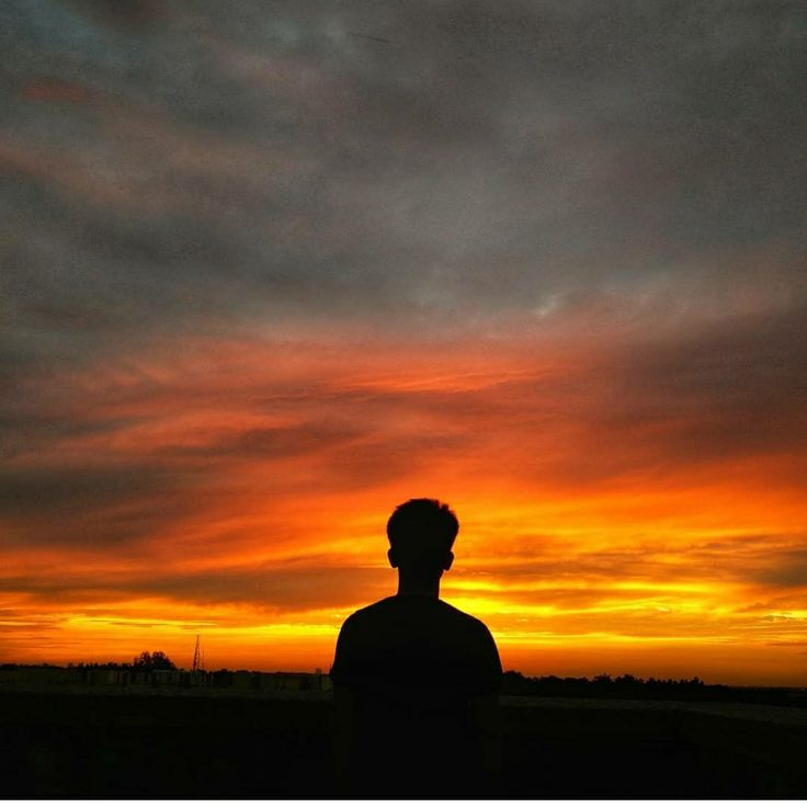 the silhouette of a man standing in front of an orange and blue sky at sunset