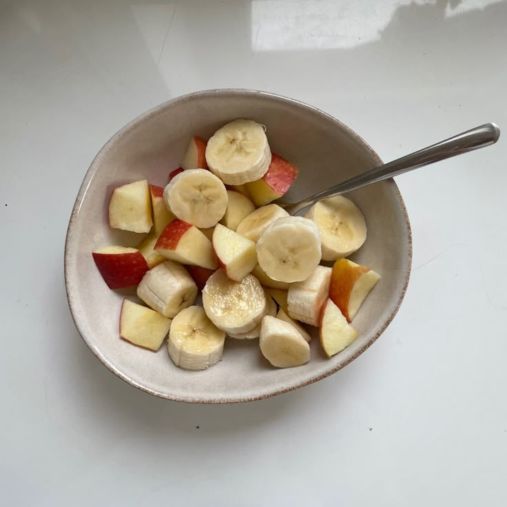 a bowl filled with sliced up bananas and apples on top of a white countertop