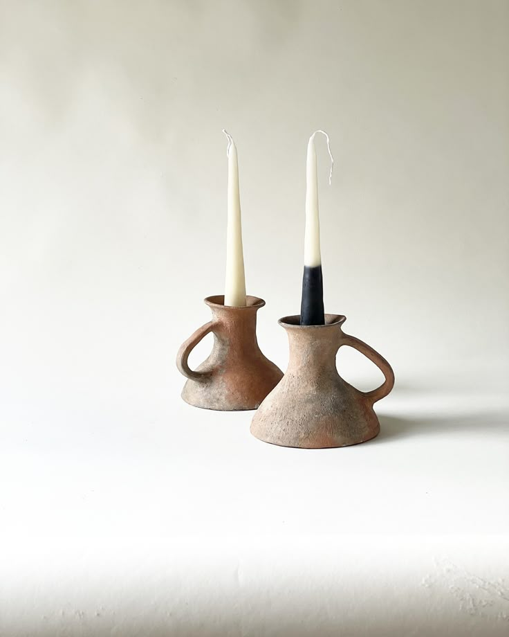 two brown vases sitting next to each other with white candles in the top one