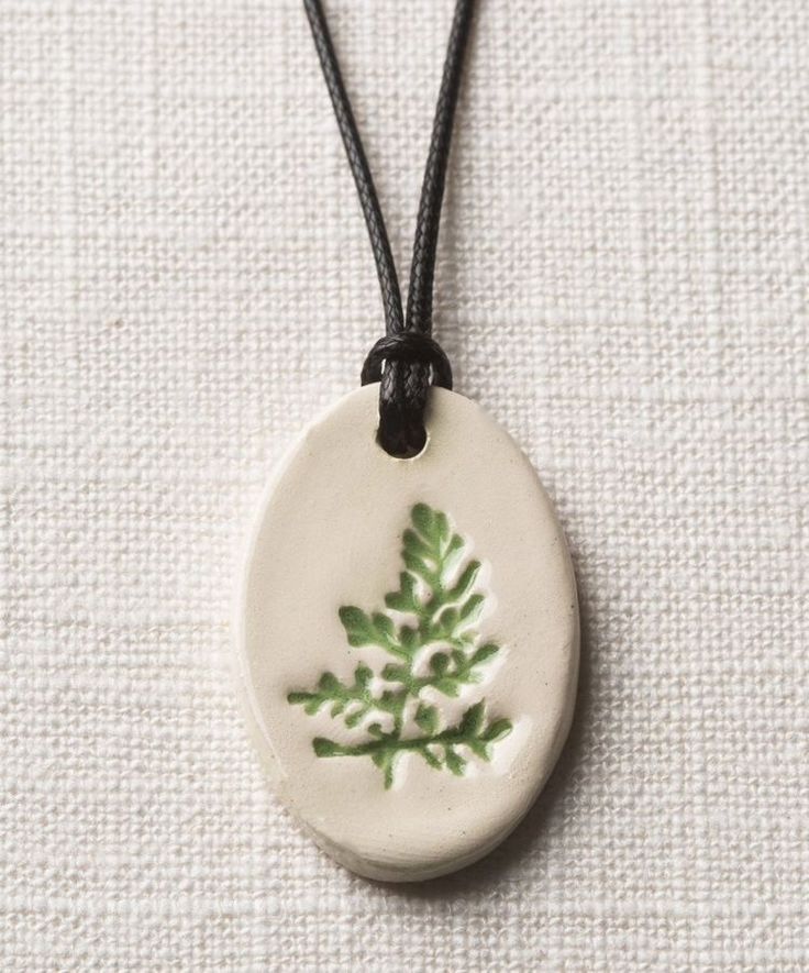 a ceramic pendant with a green leaf on it's side and a black cord