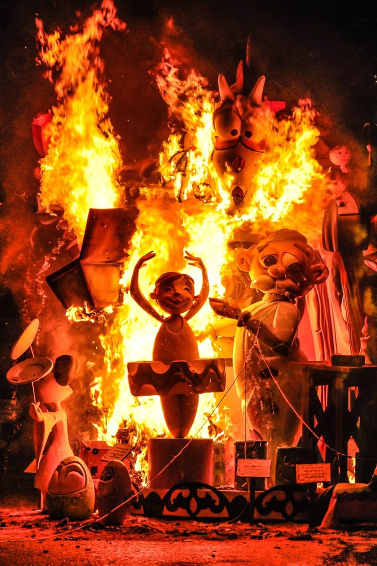 a group of people standing in front of a large fire with statues on it's sides